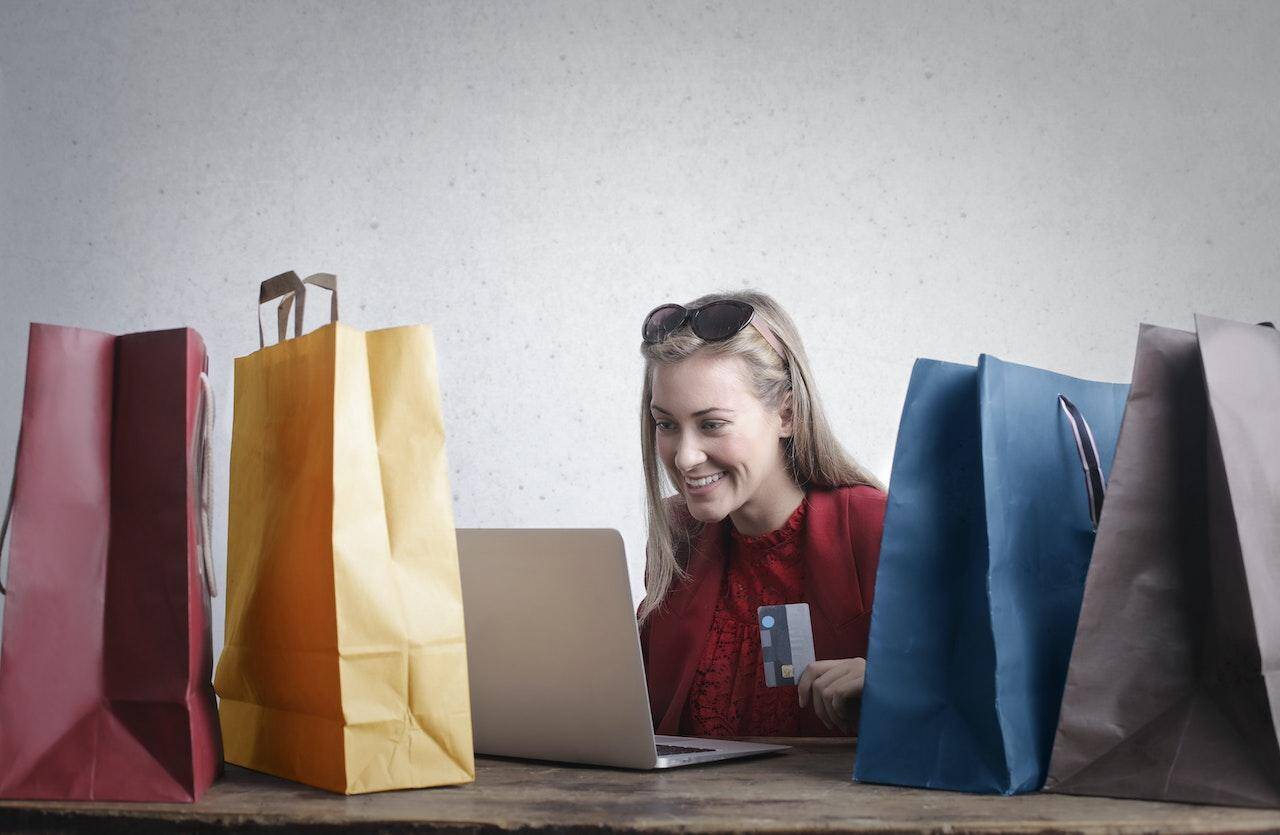 kobieta z torbami na zakupy oraz laptopem dokonuje zakupu przez Internet 